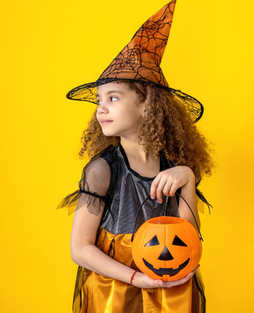 Little girl in a witch costume with a pumpkin on a yellow backgroundの写真素材