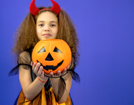 Little girl in halloween costume with a pumpkin on a blue backgroundの写真素材