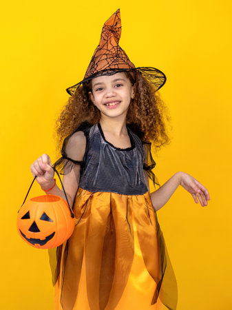 Little girl in a witch costume with a pumpkin on a yellow backgroundの写真素材