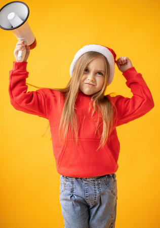 Little girl in a red sweater and Santa Claus hat on a yellow background.の写真素材