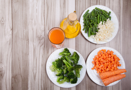 Carrots, broccoli, beans, cabbage, carrot juice and vegetable oil on a wooden tableの写真素材