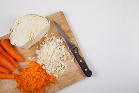 Cut raw carrots and cabbage and a knife on a white tableの写真素材