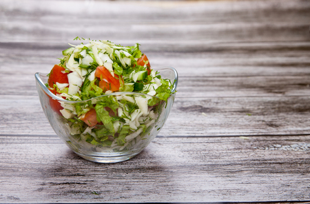 salad in a glass bowl stands on a wooden tableの写真素材