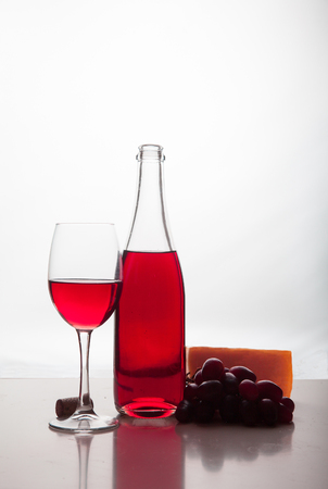 a bottle of red wine, a glass, grapes and cheese on a white tablの写真素材