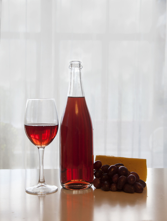 a bottle of wine, a wine glass, grapes and cheese on a white tabの写真素材