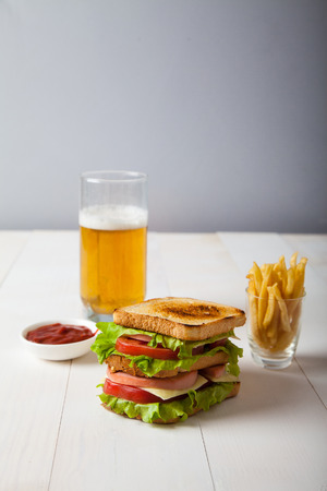 sandwich with beer, fried potatoes and sauce on white wooden bacの写真素材