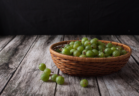 ripe gooseberry berries in a basket on a wooden backgroundの写真素材