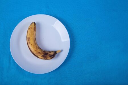One ugly banana lie on a blue porcelain plate on a blue background. copy spaes.の写真素材
