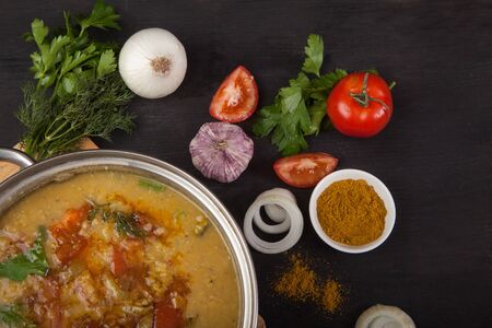 Red lentil soup with tomatoes, onions, garlic, herbs and spices in a metal pan on a black...
