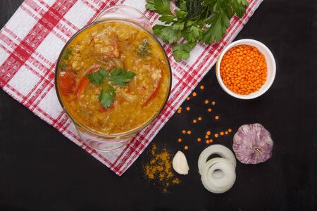 Red lentil soup with tomatoes, herbs, onions, garlic and spices in a glass plate standing on a tablecloth on a black background. Top view.の写真素材