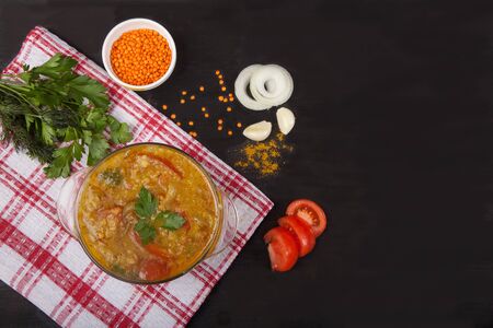 Red lentil soup with tomatoes, herbs, onions, garlic and spices in a glass plate standing on a tablecloth on a black background. Copy spaes.の写真素材