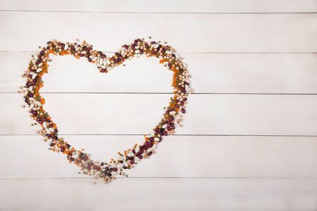 beans, lentils and beans laid out in the form of a heart on a white wooden background.の写真素材