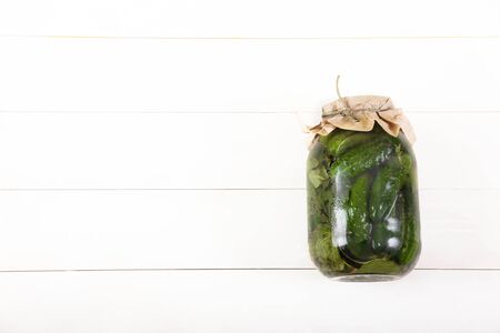 Fermented cucumbers in a glass jar on a white wooden background. Contain copy spaes