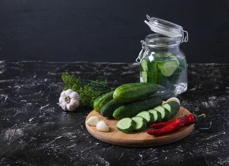 Fermented cucumbers in a glass jar, freshly chopped cucumbers, hot peppers, garlic, dill on a black background.の写真素材