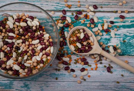 White and red beans, peas, red lentils mixed in a glass cup with a wooden spoon on a blue wooden background. horizontal.の写真素材