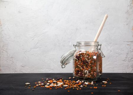 Beans, white and red, lentils green and red, peas in a glass jar on a black table on a white background. Sprinkled beans and wooden spoon. Healthy eating. Vegetarianism.の写真素材