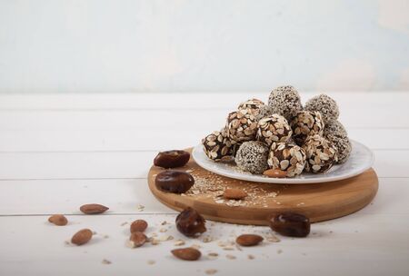Energy balls on a porcelain plate are on a wooden stand, dates and almonds are scattered around....