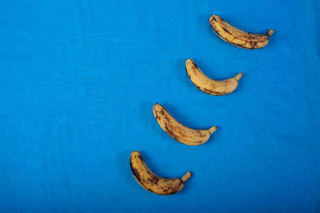 Four Ugly overripe bananas lie diagonally on a blue background. Flat lay.の写真素材
