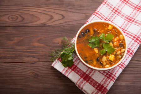 Bean soup with vegetables and cheese in a ceramic cup on a red linen napkin is on the wooden table. Italian food. Vegetarian food. Flat layの写真素材