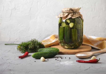 Big Jar with fermented cucumbers, salt in a wooden spoon and seasonings on a concrete background....