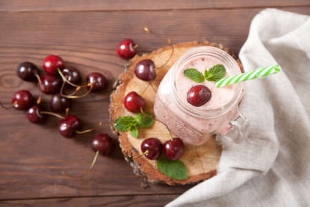 Milk and cherry smoothies in a glass mug jar, next to a cherry, a linen napkin on a wooden stand. Flat lay.の写真素材