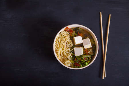 Japanese soup with vegetables, pasta, tofu cheese, chopsticks on a black background. Flat layの写真素材