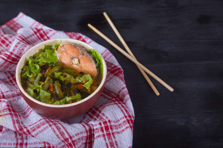 Japanese soup with salmon, green beans, herbs and bamboo chopsticks on a red napkin on a black background. Copy spaesの写真素材