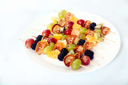 Dessert on skewers from minipuncakes, blackberries, vgrada and kiwi on a plate on a light concrete backgroundの写真素材