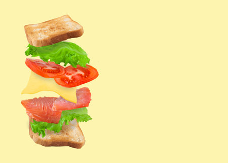 Flying sandwich with salmon, cheese and tomatoes isolated on a yellow background. Fast food concept....