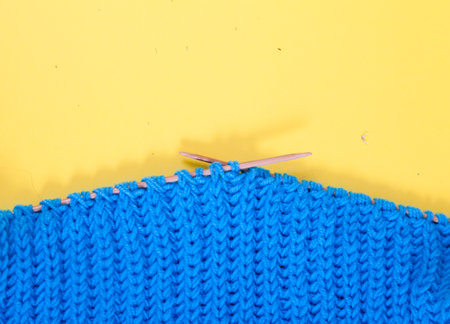 Knitted blue scarf lies on a yellow background. Handmade concept.Copy space