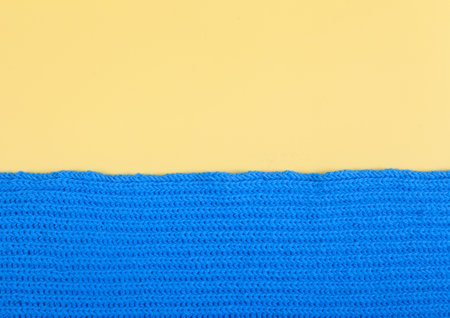 A fragment of a blue scarf knitted by hand lies on a yellow background. Handmade concept