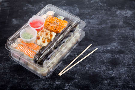 Two plastic boxes with sets of rolls, wasabi and ginger, bamboo chopsticks on a black background.の写真素材