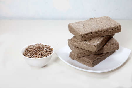 Briquettes of halva from sunflower seeds are on a white plate. Sunflower seeds in a porcelain cup are next to each other.の写真素材