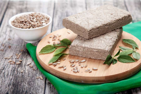 Briquettes of sunflower halva, sunflower seeds and green leaves lie on a wooden board on a green...