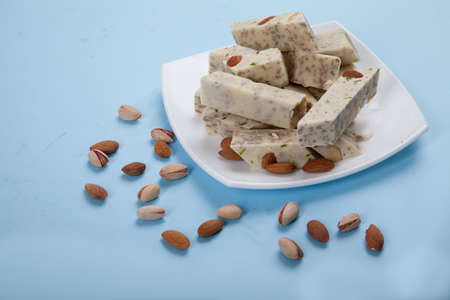 Halva made from sunflower seeds, almonds and pistachios lies on a plate against a blue background. Pistachios and almonds are scattered side by side.の写真素材