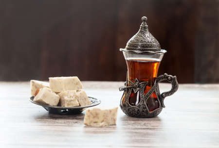 Turetius a glass of tea, a metal spoon and sunflower halva with almonds and pistachios stands on a wooden background.の写真素材