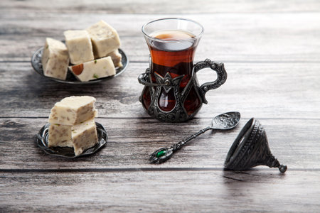 Turetius a glass of tea, a metal spoon and sunflower halva with almonds and pistachios stands on a wooden background.の写真素材