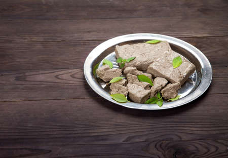 Briquettes and pieces of halva and green basil leaves lie on a metal plate on a wooden background. Copy spaes.の写真素材
