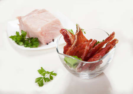 Jerky in a cup and raw meat with herbs on a white plate.の写真素材