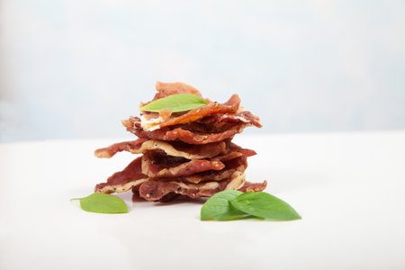 Pieces of jerky are in a pile, decorated with basil leaves on a white background.の写真素材