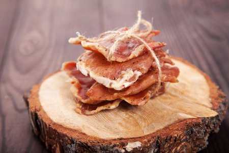 Pieces of jerky in a pile tied with twine lie on a cut of a tree on a wooden background.の写真素材