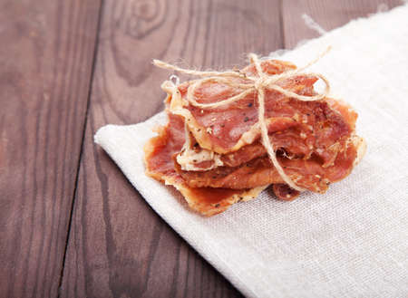 Pieces of jerky in a pile tied with twine lie on a linen napkin on a wooden background.の写真素材