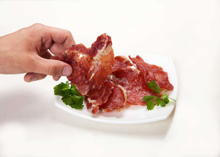 A man's hand takes a piece of jerky from a white plate.の写真素材