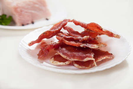 Jerky in a cup and raw meat with herbs on a white plate.の写真素材