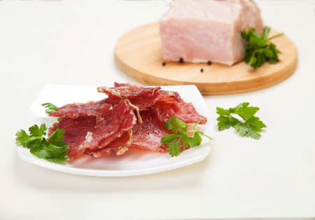 Jerky in a cup and raw meat with herbs on a white plate.の写真素材