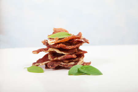 Pieces of jerky are in a pile, decorated with basil leaves on a white background.の写真素材