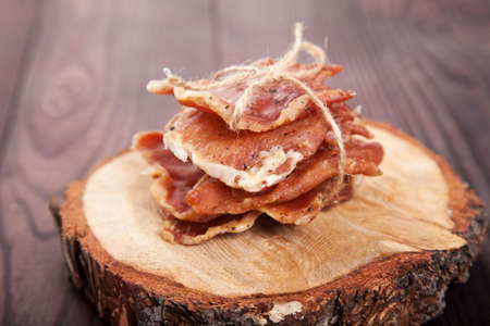 Pieces of jerky in a pile tied with twine lie on a cut of a tree on a wooden background.の写真素材