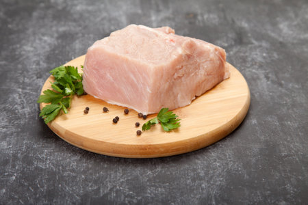 A piece of raw meat with herbs lies on a wooden cutting board on a black background.の写真素材