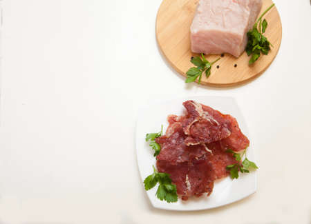 Jerky in a cup and raw meat with herbs on a white plate. Copy spaes.の写真素材