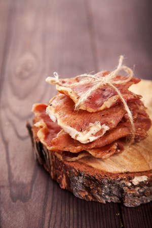 Pieces of jerky in a pile tied with twine lie on a cut of a tree on a wooden background. Vertically.の写真素材